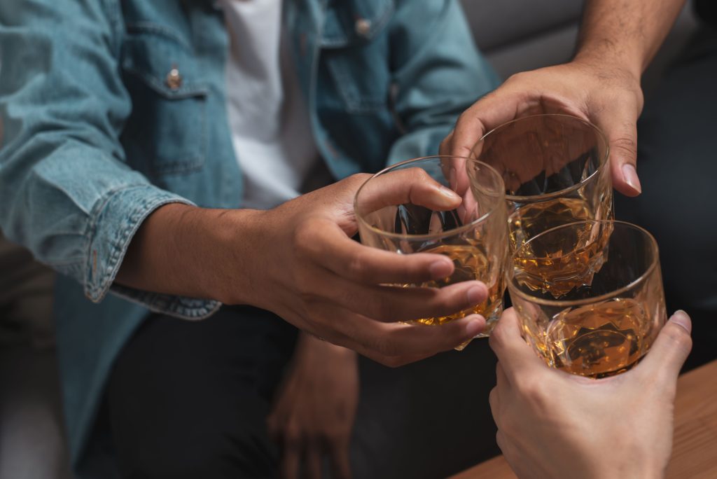 Three people raising whiskey glasses in a toast, celebrating with clinks