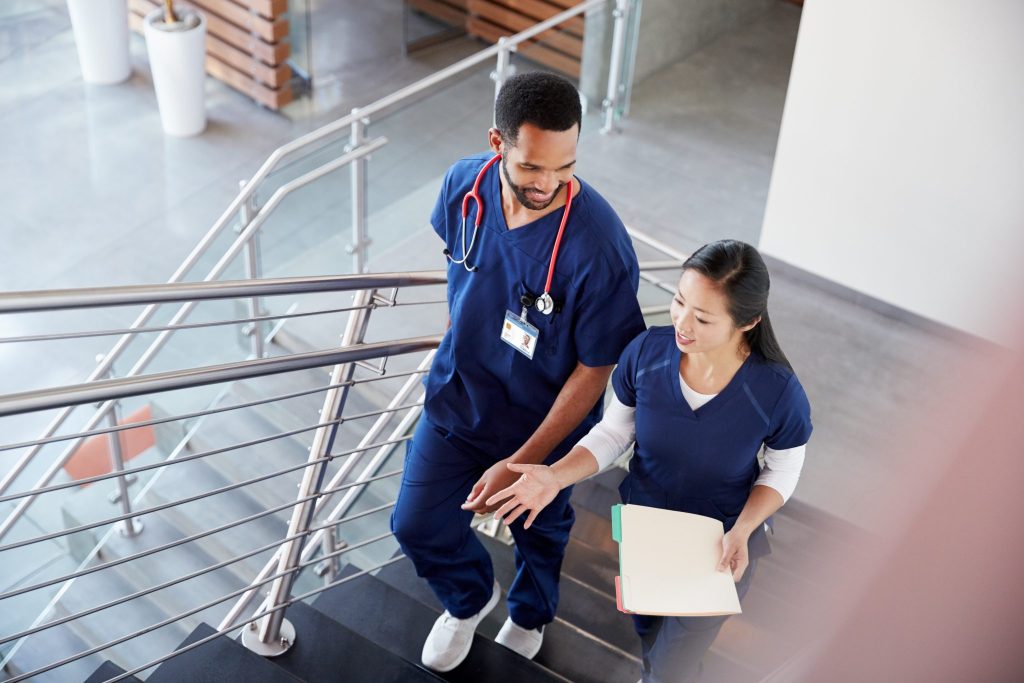 Two nurses walking down stairs, one holding a folder, engaged in conversation