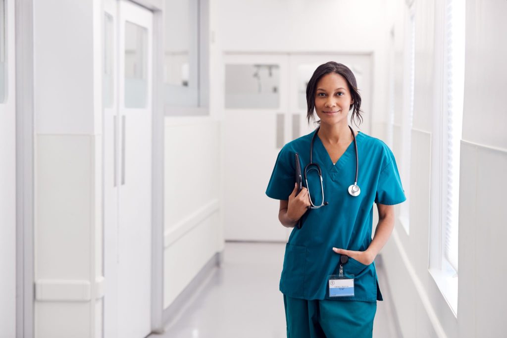 A female nurse in a hallway, wearing a stethoscope and with her hand in her pocket
