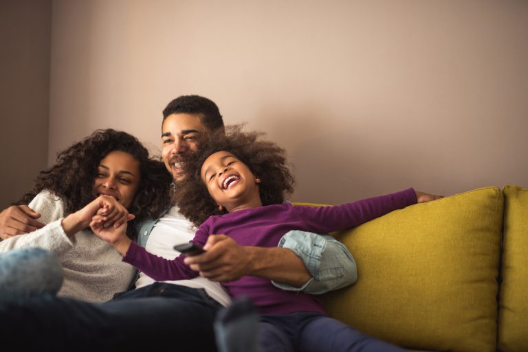 A happy family sitting on a couch, enjoying their time together with a remote control nearby