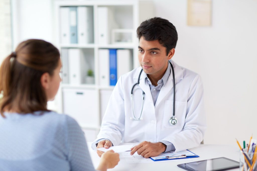 A doctor conversing with a patient in a medical office, handing over a paper to the woman