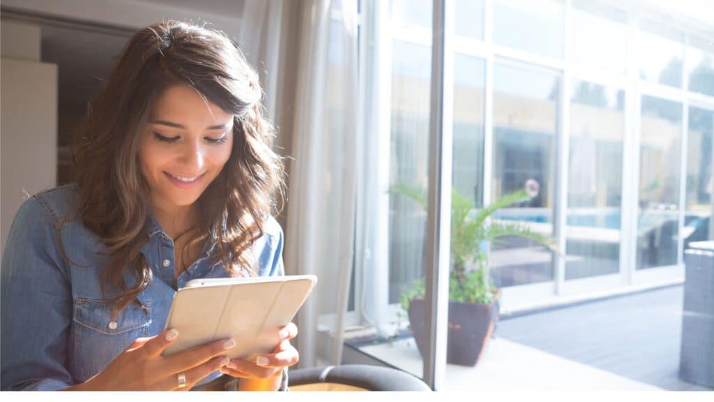 A smiling woman sitting at a table, looking at a tablet